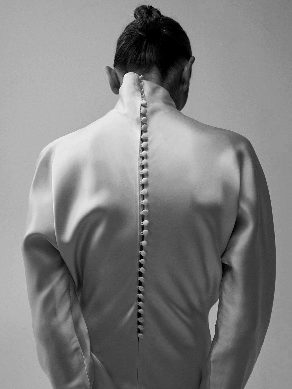 Back of a white satin garment with a long row of covered buttons along the spine